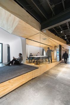 a person sitting on the floor in front of a glass wall with people walking by