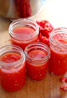 four jars filled with red sauce sitting on top of a wooden table