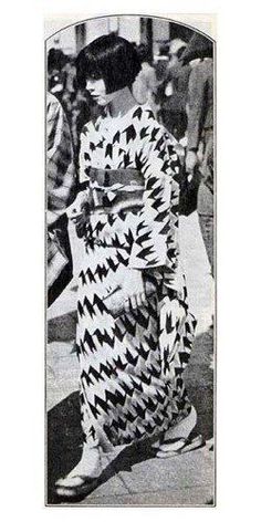 an old black and white photo of a woman in a kimono walking down the street