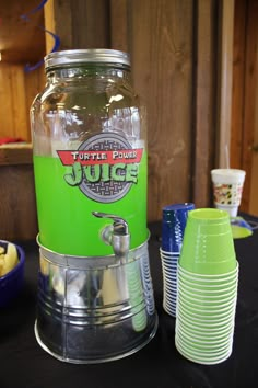 a green juice dispenser sitting on top of a table next to cups