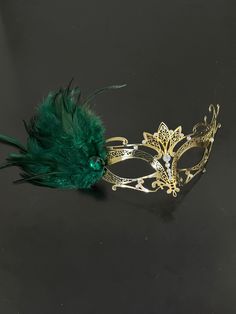 This mask is crafted in the tradition of Venetian masquerade, exuding timeless elegance and grace. The graceful green feathers add a touch of enchantment and create a mesmerizing aura around you. The sparkling emerald green stones accentuate the mask's design, illuminating your face with radiant brilliance. Whether you're attending a masquerade party, ball, or gala, this mask is the perfect choice! Age Group/Gender - Adult/Womens Size/Type - One size fits all adults Mask Color - Gold Rhinestone Color - Clear Mask Material - Metal Special Features - Green feathers Personalization - Not available Masquerade Mask Green And Gold, Masquerade Mask Women, Rhinestone Mask, Gold Masquerade Mask, Black Masquerade Mask, Clear Mask, Green Feathers, Emerald Green Stone, Feather Mask