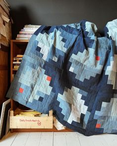 a bed with a blanket on top of it next to a wooden box filled with books