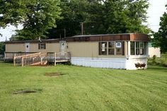 a mobile home sits in the middle of a grassy area with trees and grass around it