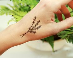 a person's hand with a small tattoo on it and some plants in the background