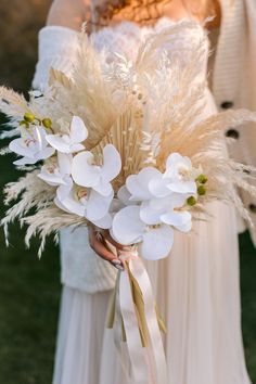 a woman in a white dress holding a bouquet with flowers and feathers on her arm