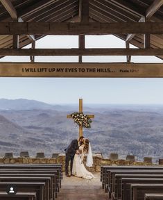 a bride and groom kissing in front of a cross at the top of a hill