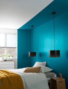 a bedroom with blue walls and white bedding, two lamps hanging from the ceiling