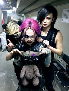 three women with pink hair and black leather clothes are posing for the camera while one woman is holding a teddy bear