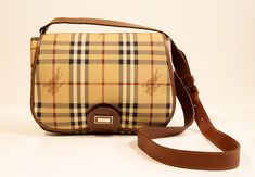 A vintage Burberry saddle crossbody bag made of vinyl coated canvas with the classic Burberry check. The bag features brown leather trim and gold toned hardware. The interior consists of two major compartments divided with a zipped pocket.   The shoulder strap is in length adjustable max. 116 cm. The bag has minor signs of use in relation to its age and it is in very good vintage condition.   Measurements Width:26 cm Height:20 cm Depth:9 cm This item will be shipped by a regular shipping carrier Everyday Plaid Bag With Adjustable Strap, Brown Tapestry Shoulder Bag With Detachable Strap, Plaid Shoulder Bag With Adjustable Strap For Daily Use, Vintage Brown Monogram Canvas Shoulder Bag, Saddle Crossbody Bag, Burberry Vintage Crossbody Bag, Vintage Burberry, Check In, Leather Trims