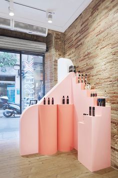 a pink display case with bottles on it in front of a brick wall