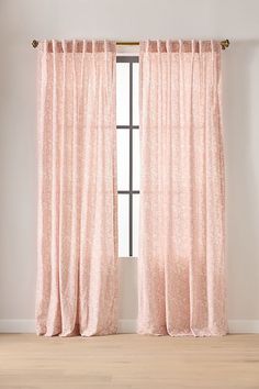 a pink curtain hanging in front of a window with white walls and wooden flooring