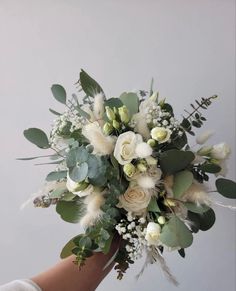 a bridal bouquet in someone's hand with white flowers and greenery on it