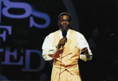 a man in an orange vest and white shirt holding a microphone while standing on stage