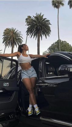 a woman leaning on the door of a car with palm trees in the back ground