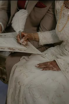 a man and woman sitting next to each other in wedding attire holding papers with writing on them