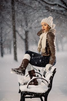 a woman is sitting on a bench in the snow wearing boots and a hat with fur