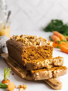 a loaf of carrot cake on a cutting board next to carrots and other vegetables