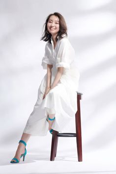 a woman sitting on top of a wooden chair in front of a white background wearing blue heels