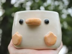 a close up of a person holding a ceramic object with two eyes and nose shapes