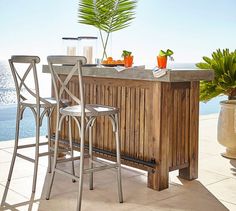 an outdoor bar with two chairs next to it and a potted plant on the counter