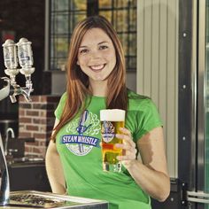 a woman in a green shirt is holding a beer glass and smiling at the camera