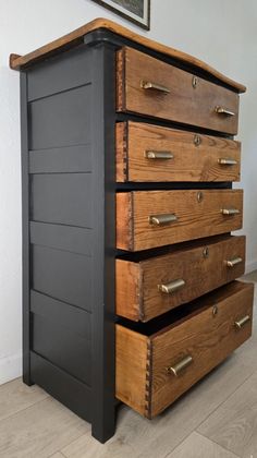 a wooden dresser with five drawers and brass pulls on the bottom drawer, against a white wall