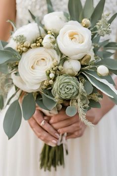 a bride holding a bouquet of white flowers and greenery