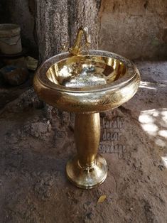 a gold pedestal sink sitting on top of a stone floor next to a large tree