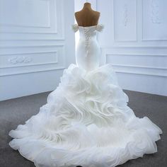 a white wedding dress with ruffled skirt on display in front of a mannequin