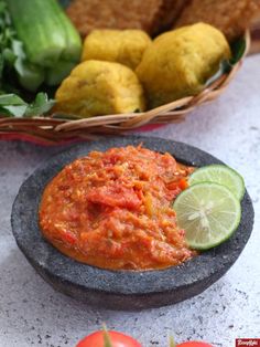 there is a bowl of sauce next to some tomatoes and cucumbers