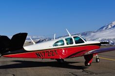 a small red and white plane sitting on top of an airport tarmac with snow covered mountains in the background