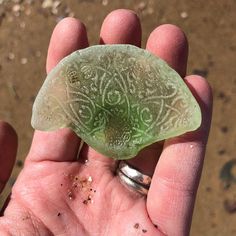 a hand holding a piece of green glass in it's left palm, with dirt on the ground behind it