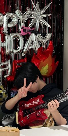 a man sitting at a table with a guitar in front of him and balloons behind him