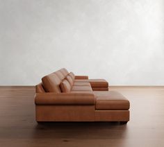 a brown leather couch sitting on top of a wooden floor next to a white wall