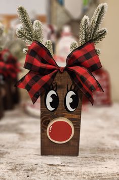 a wooden reindeer head with red nose and plaid bow on it's head, sitting on a table