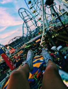 a person standing in front of a ferris wheel at an amusement park with their feet up