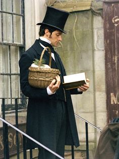 a man wearing a top hat and holding a book in front of a building with wrought iron railings