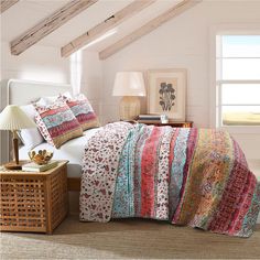 a bedroom with white walls and wooden beams has a large bed covered in colorful quilts