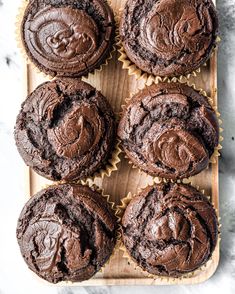 six chocolate cupcakes sitting on top of a wooden tray