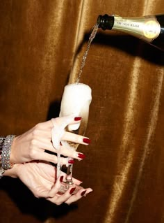 a woman pouring champagne into a glass with her hand and red nail polish on it