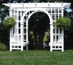 a white garden arbor with chairs and potted plants on the lawn in front of it