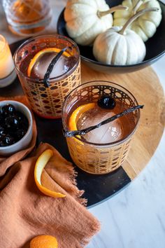 two glasses filled with orange slices and black olives on top of a wooden table