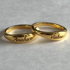 two yellow gold wedding rings with names engraved on the sides and hearts at the bottom