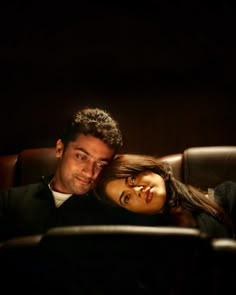 a man sitting next to a woman on top of a brown leather couch in a dark room