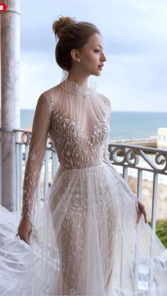 a woman in a wedding dress is standing on a balcony near the ocean and looking off into the distance