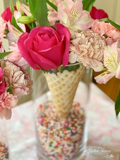 a vase filled with lots of pink flowers and sprinkles on top of a table