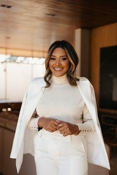 a woman in white pants and jacket smiling at the camera with her hand on her hip