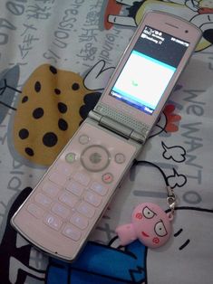 a cell phone laying on top of a bed next to a pink pig keychain