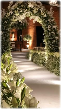 an archway with white flowers and greenery in front of a brick building at night