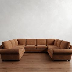 a brown sectional couch sitting on top of a wooden floor next to a white wall